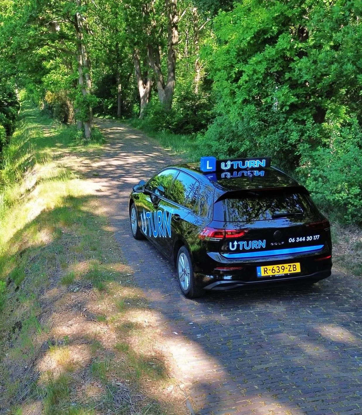 Zwarte rijschoolauto met Uturn logo op bospad