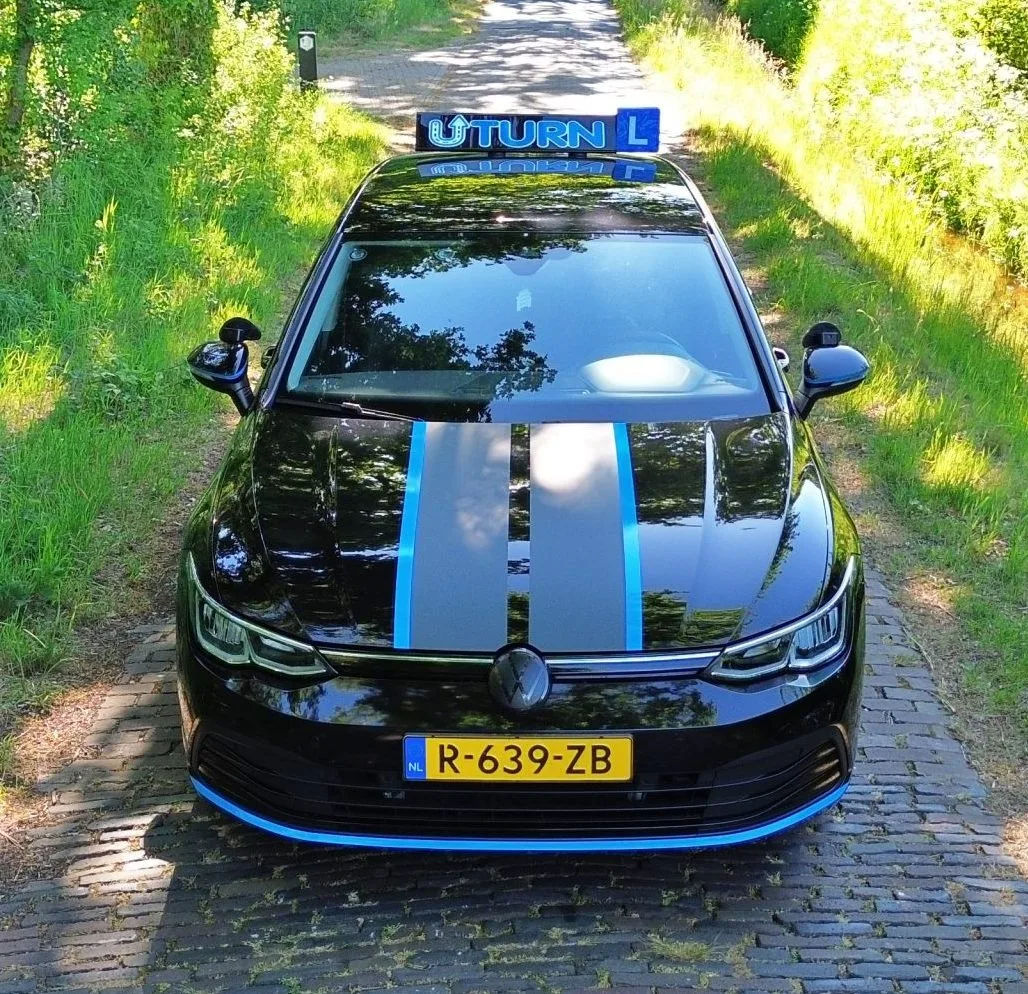 Zwarte Uturn rijschoolauto van voren op klinkerpad in bos