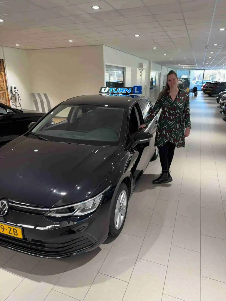 Instructrice loopt naar zwarte rijschoolauto in showroom
