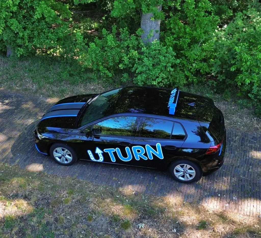 Zwarte rijschoolauto met Uturn logo geparkeerd in bosrijke omgeving van boven